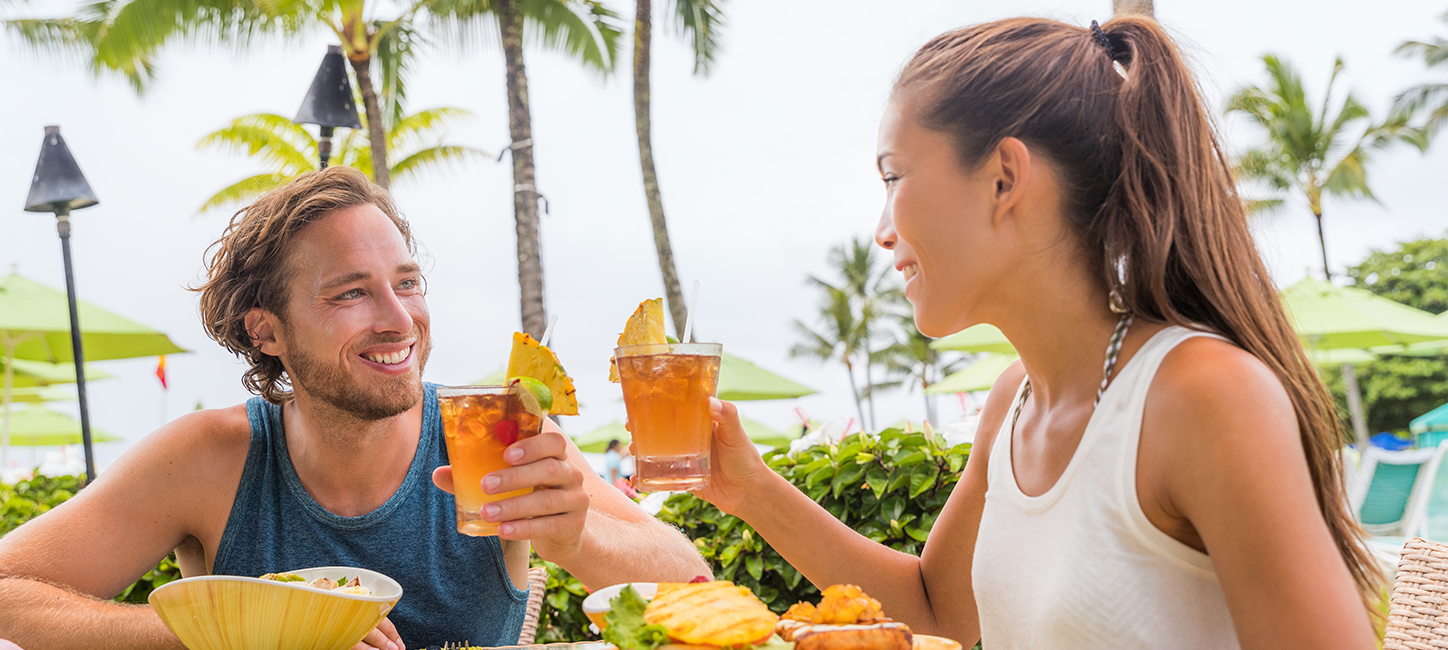 a man and women cheering cocktails with palm trees in the background