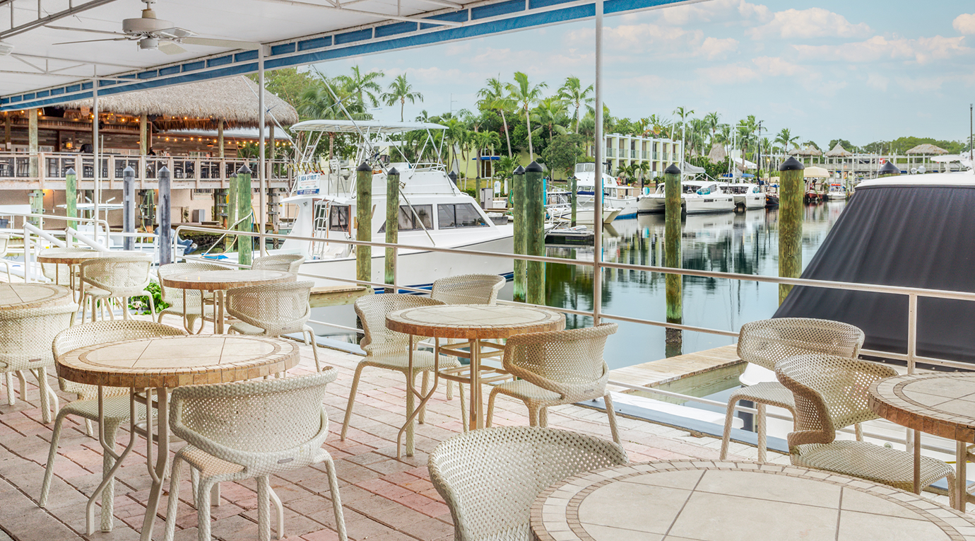 A deck with tables and chairs overlooking a marina.