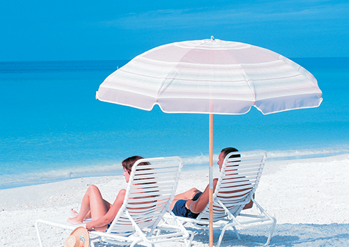 Two people sitting under an umbrella on a beach.