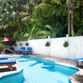 A pool with blue lounge chairs and a white fence.