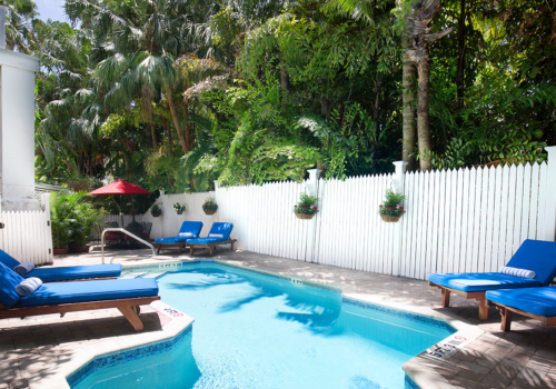 A pool with blue lounge chairs and a white fence.