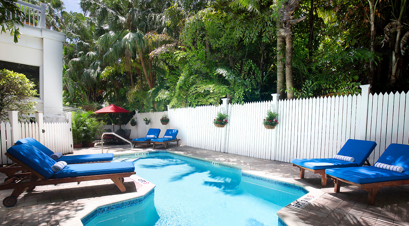 A pool with blue lounge chairs and a white fence.