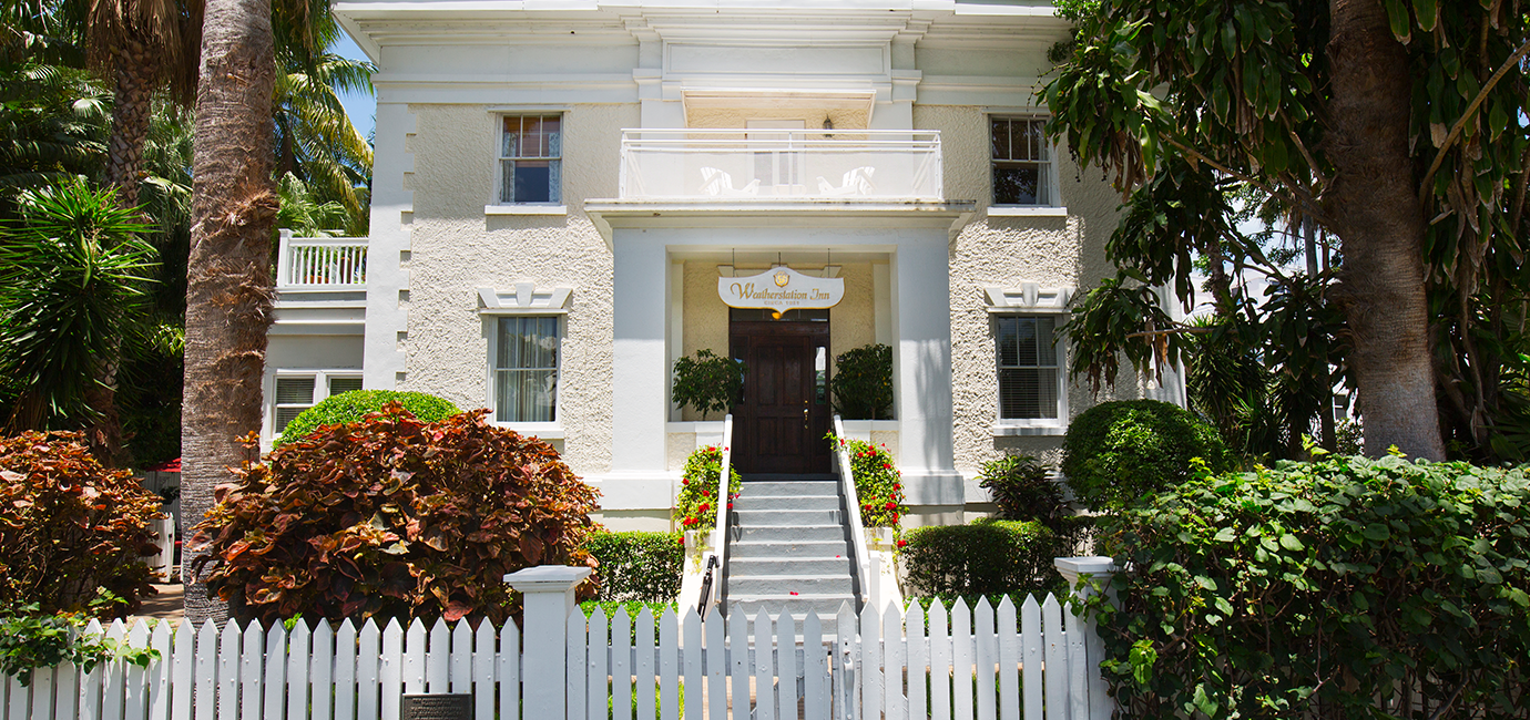 A white house with palm trees and a white picket fence.