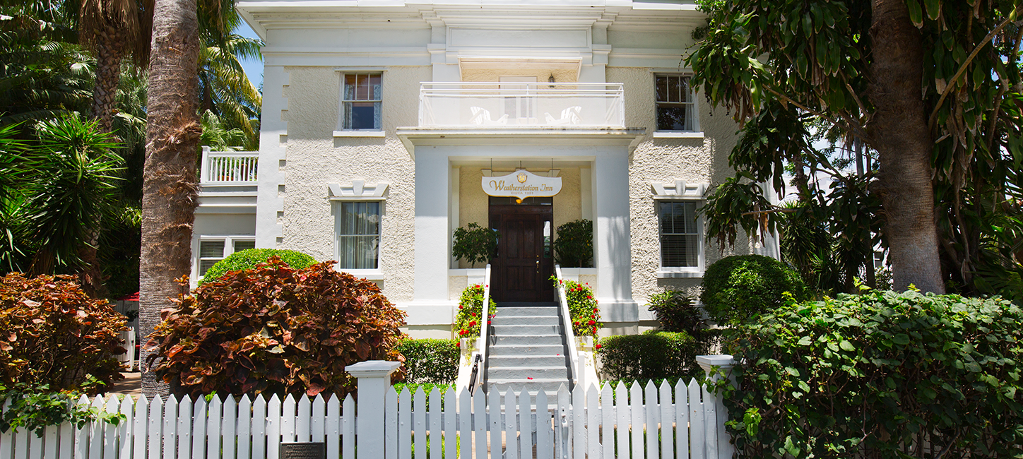 A white house with palm trees and a white picket fence.