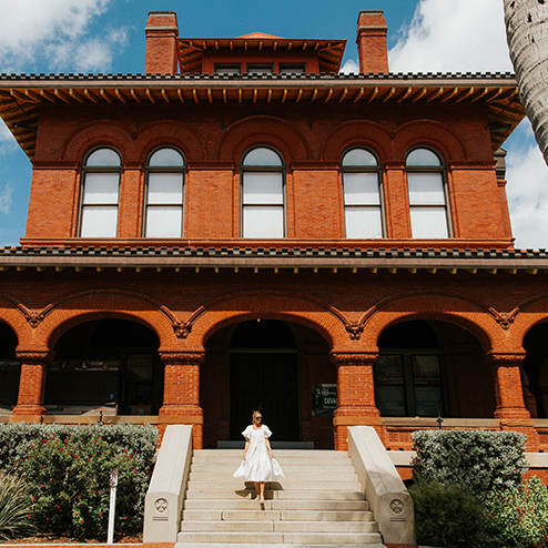A woman in a white dress standing on the steps of a building.