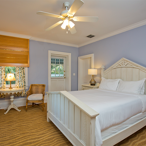 A white bed in a bedroom with a ceiling fan.
