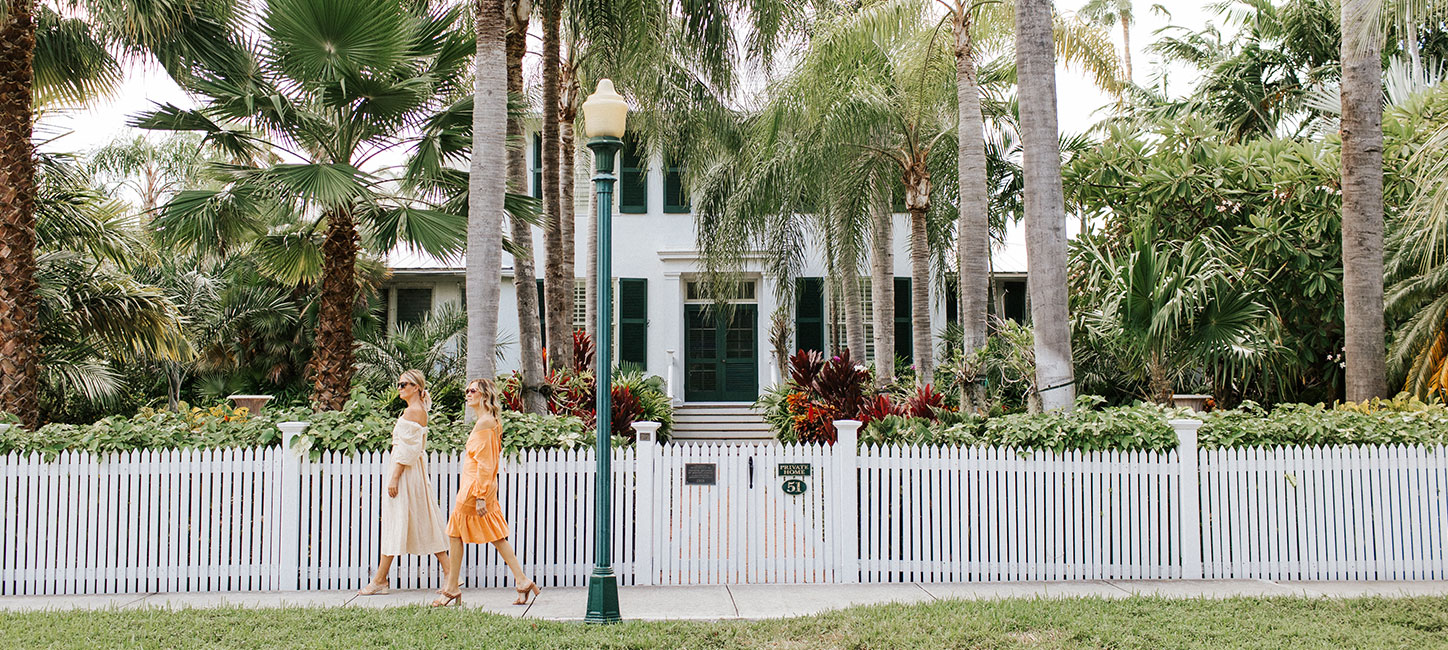 Two women standing in front of a white picket fence.