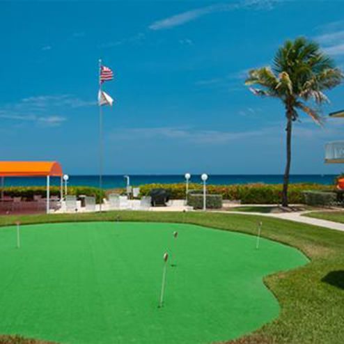 A golf course with a flag and palm trees.