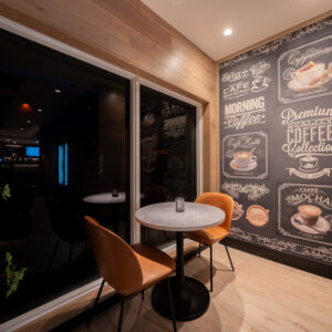 Interior of a modern café featuring a small round table, two chairs, and a decorative wall with chalkboard-style coffee-themed artwork.