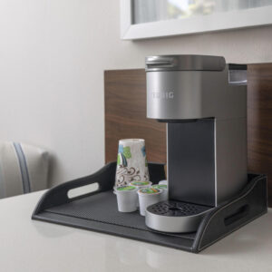 A keurig coffee maker on a tray with k-cup pods and a takeaway cup next to it on a kitchen counter.