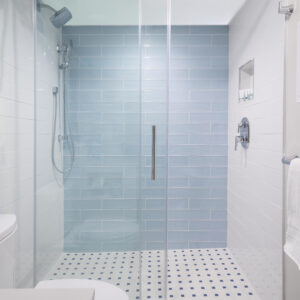 Modern bathroom interior featuring a glass shower stall with blue tiles, white floor, and visible toilet on the left.