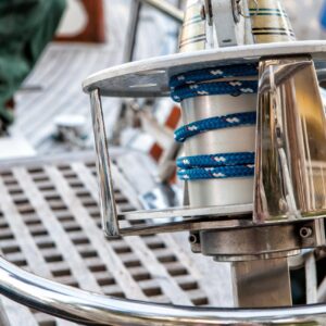 Close-up of a yacht's steering wheel with coiled blue and white rope, focusing on the metallic details and nautical equipment.