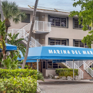Exterior view of marina del mar building with blue awnings and white staircases surrounded by tropical plants.