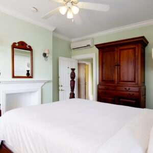A neatly arranged bedroom with a large bed, wooden furniture, and a ceiling fan, featuring light green walls and white trim.