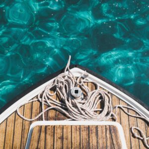 The bow of a boat with coiled ropes on a wooden deck, floating on clear, turquoise water.