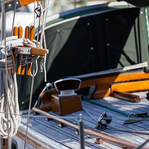 Close-up of a sailboat's deck showing coiled ropes, winches, and wooden fixtures with a green cover in the background.